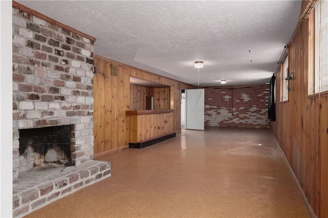 unfurnished living room with wooden walls, a brick fireplace, and a textured ceiling