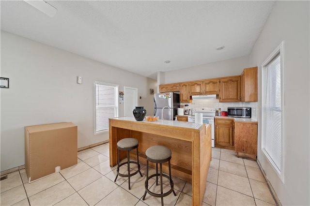 kitchen with appliances with stainless steel finishes, a kitchen island with sink, light tile patterned floors, and decorative backsplash