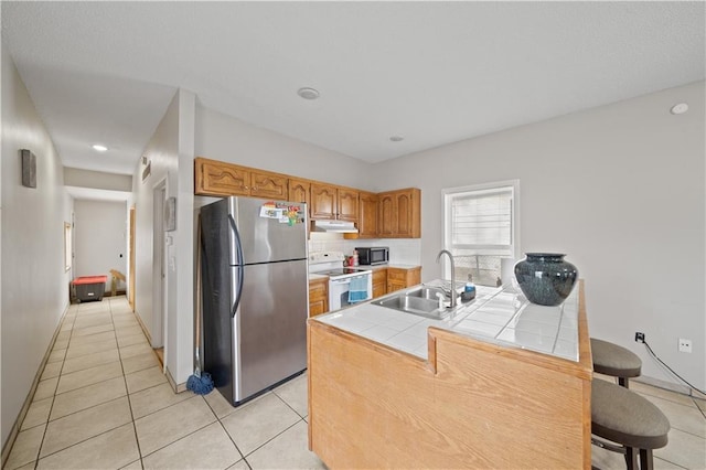 kitchen with electric stove, sink, stainless steel fridge, tile counters, and light tile patterned flooring