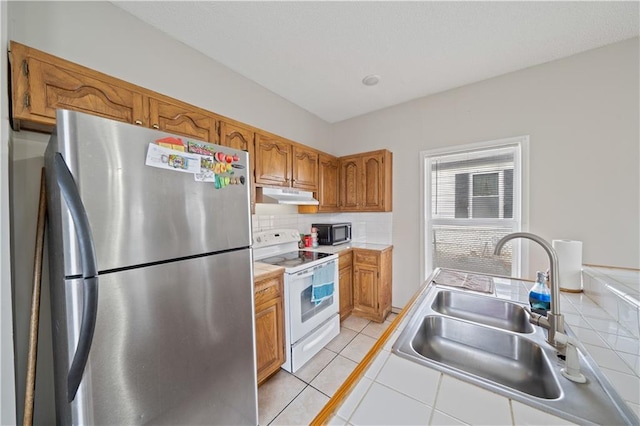 kitchen featuring tasteful backsplash, sink, stainless steel fridge, light tile patterned floors, and white range with electric cooktop