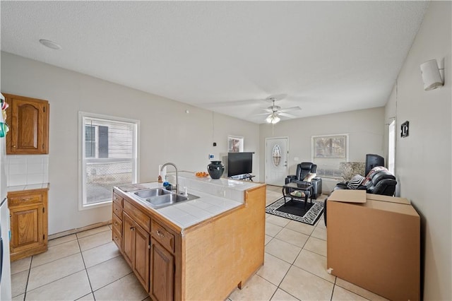 kitchen with tile countertops, a kitchen island with sink, sink, and light tile patterned floors