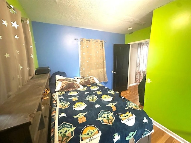 bedroom featuring a textured ceiling, a closet, wood finished floors, and baseboards