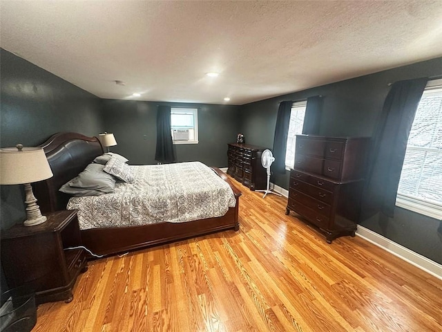 bedroom featuring cooling unit, baseboards, a textured ceiling, and light wood finished floors