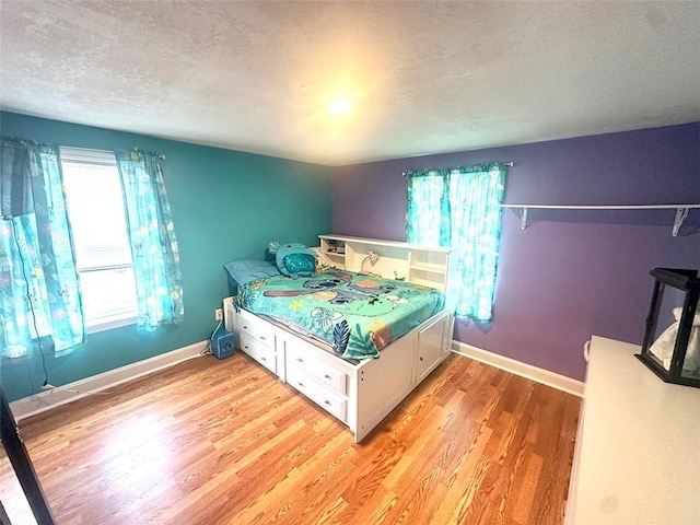 bedroom featuring light wood-style flooring, baseboards, and a textured ceiling