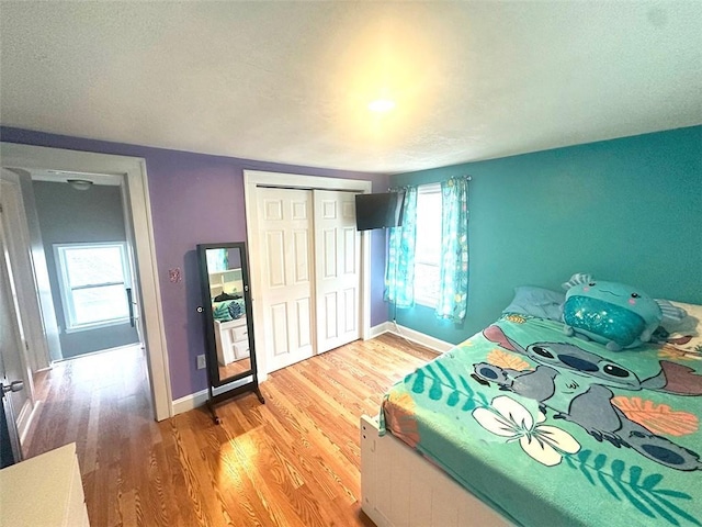 bedroom featuring a closet, multiple windows, baseboards, and wood finished floors