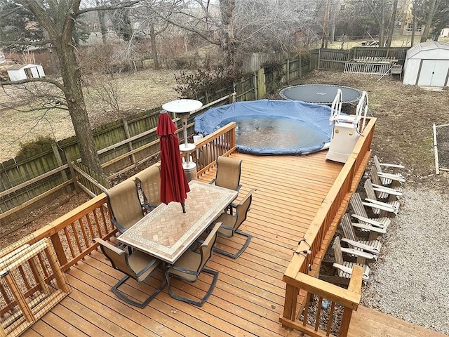 wooden terrace featuring outdoor dining area, a fenced backyard, an outdoor structure, a covered pool, and a shed