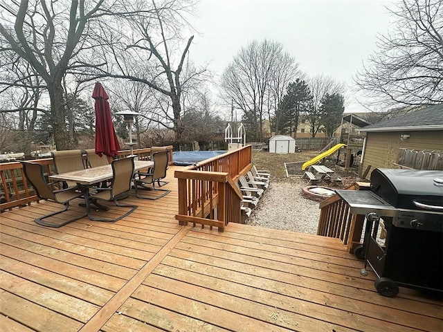 deck with a grill, a storage unit, playground community, an outdoor structure, and outdoor dining space