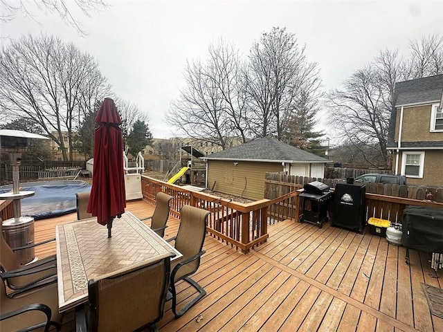 deck with outdoor dining area, a fenced backyard, a grill, and a playground