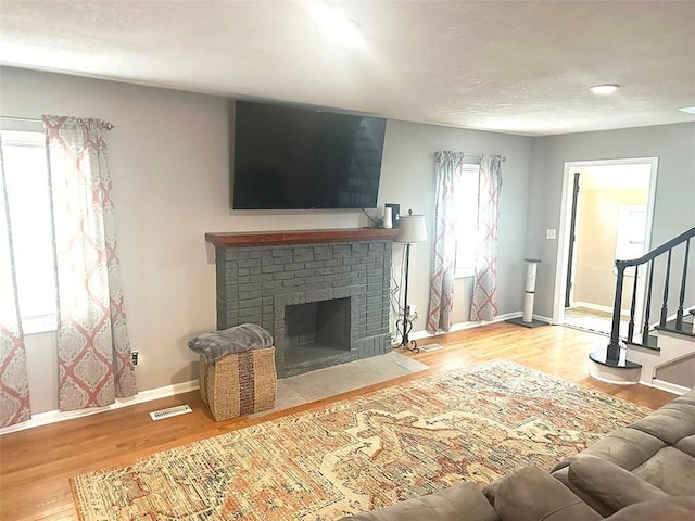 living area with baseboards, visible vents, stairway, wood finished floors, and a brick fireplace