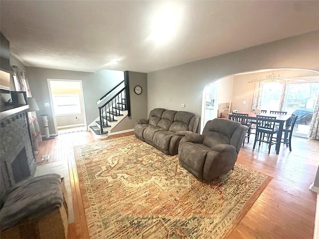 living area with arched walkways, a fireplace, stairway, and wood finished floors