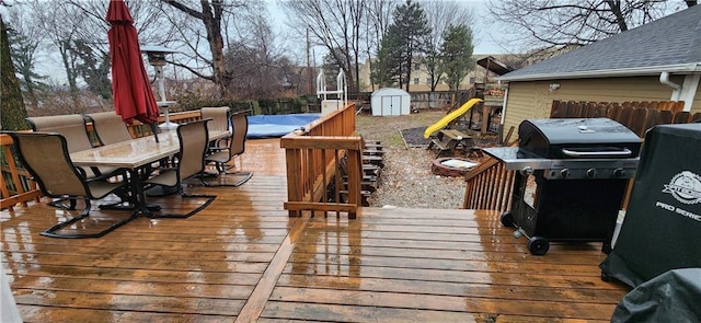 wooden deck featuring outdoor dining area, a playground, a storage shed, an outdoor structure, and grilling area