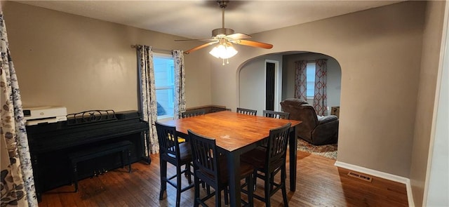 dining space featuring arched walkways, visible vents, baseboards, a ceiling fan, and dark wood finished floors