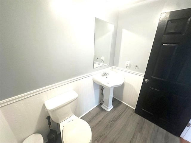 bathroom with a wainscoted wall, wood finished floors, and toilet