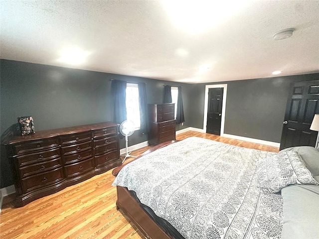 bedroom with light wood-style floors, baseboards, and a textured ceiling