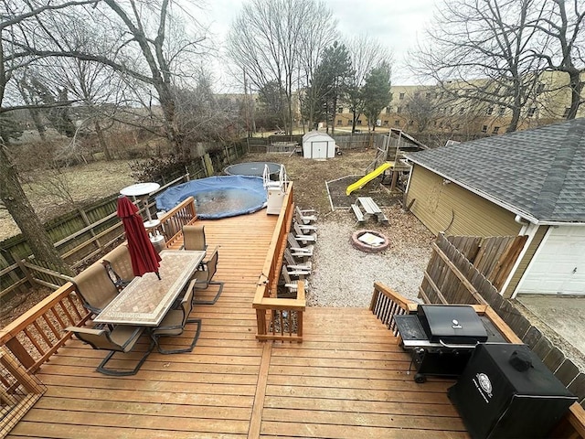 wooden deck featuring a fire pit, a fenced backyard, an outbuilding, outdoor dining area, and a shed