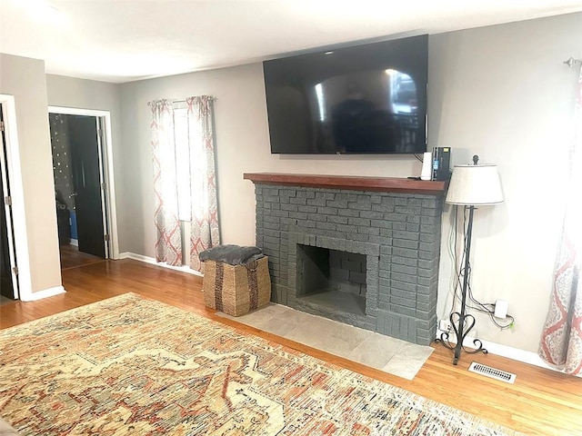 living room featuring baseboards, a fireplace, visible vents, and wood finished floors