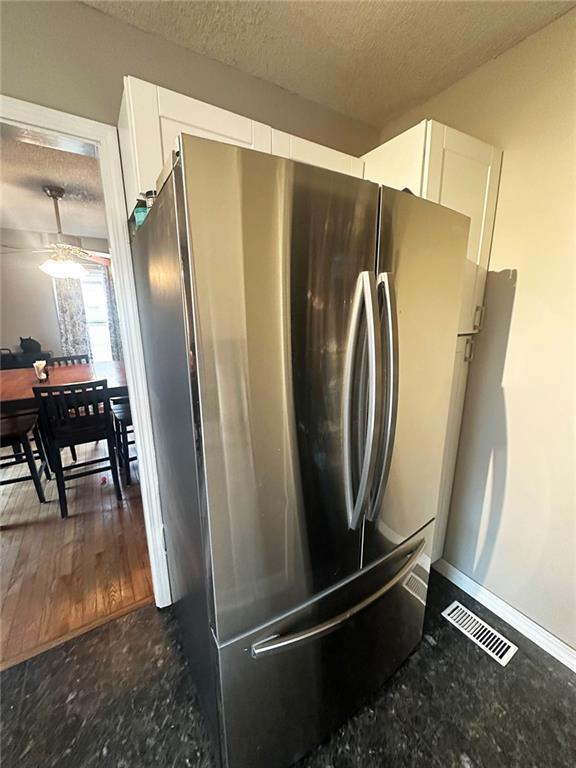 kitchen with visible vents, dark stone counters, white cabinets, freestanding refrigerator, and a textured ceiling