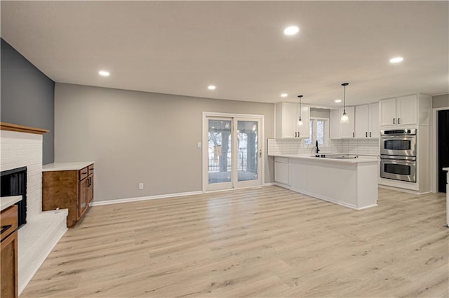 kitchen with white cabinetry, decorative light fixtures, kitchen peninsula, stainless steel double oven, and a fireplace