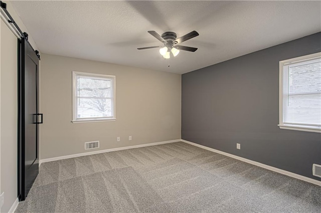 unfurnished room featuring ceiling fan, light colored carpet, a barn door, and a healthy amount of sunlight