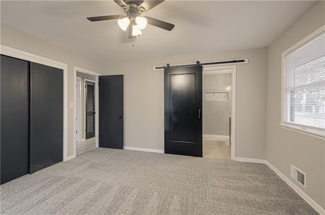 unfurnished bedroom featuring light carpet, a closet, a barn door, and ensuite bathroom