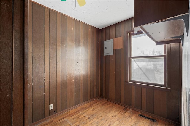 spare room featuring ceiling fan, light hardwood / wood-style flooring, and wood walls