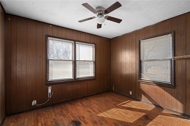 empty room with ceiling fan, hardwood / wood-style floors, and wood walls