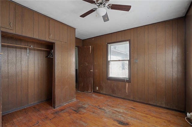 unfurnished bedroom with hardwood / wood-style flooring, ceiling fan, wooden walls, and a closet