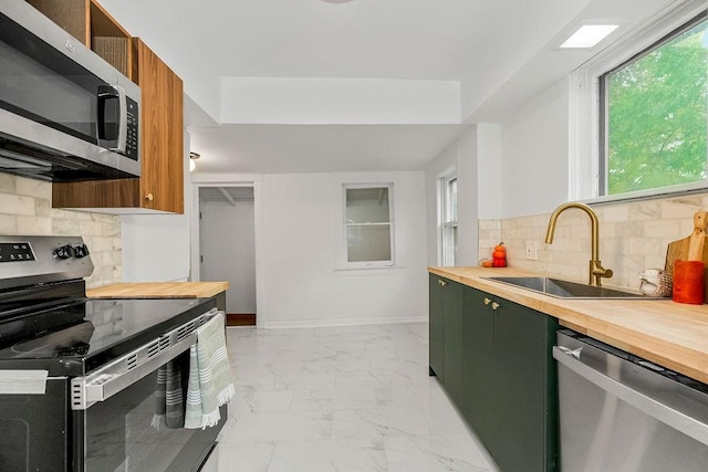 kitchen with sink, green cabinets, appliances with stainless steel finishes, wood counters, and decorative backsplash