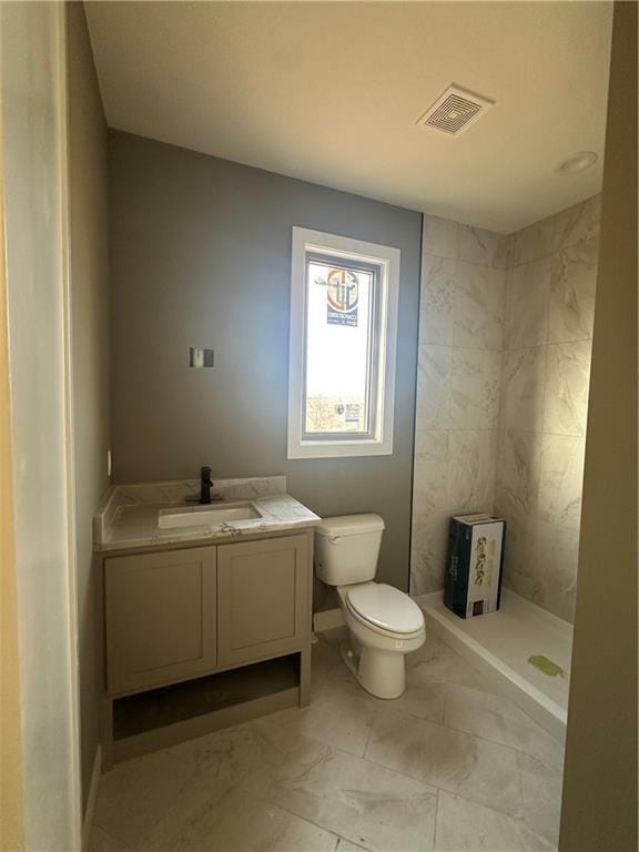 bathroom with vanity, toilet, and tiled shower