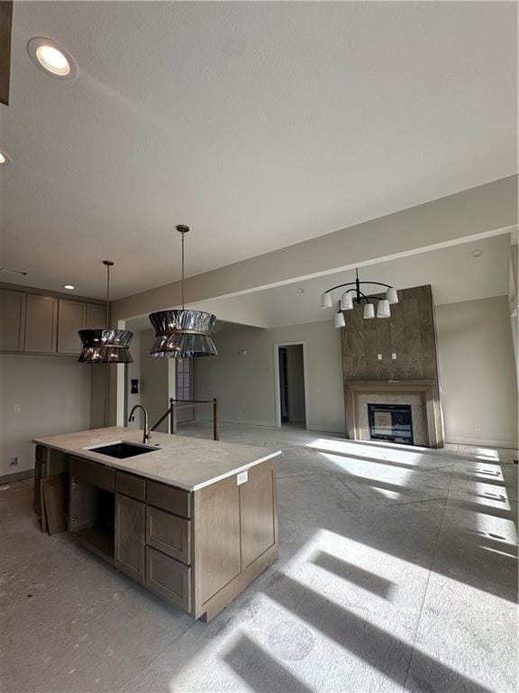 kitchen featuring a tile fireplace, sink, a kitchen island with sink, and decorative light fixtures