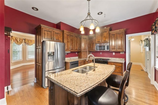 kitchen featuring sink, appliances with stainless steel finishes, light stone countertops, an island with sink, and decorative light fixtures