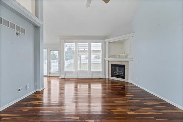 unfurnished living room featuring dark wood-type flooring, ceiling fan, a tiled fireplace, and high vaulted ceiling