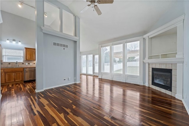 unfurnished living room with sink, a tile fireplace, ceiling fan, high vaulted ceiling, and dark hardwood / wood-style flooring