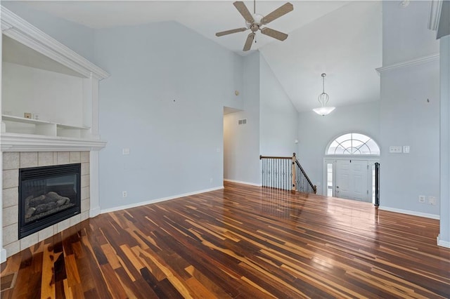 unfurnished living room featuring dark wood-type flooring, ceiling fan, a tiled fireplace, and high vaulted ceiling