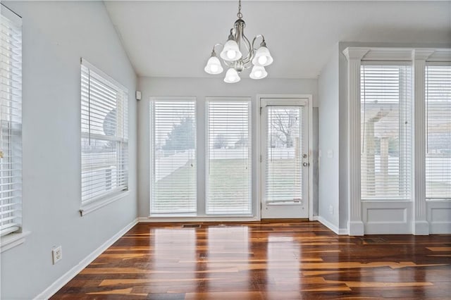 unfurnished dining area featuring dark wood-type flooring, plenty of natural light, an inviting chandelier, and vaulted ceiling