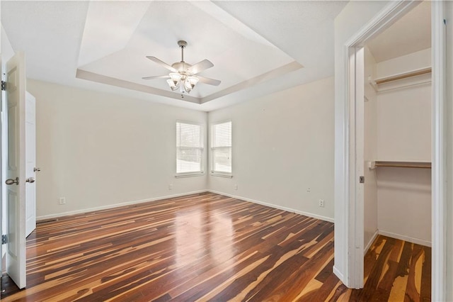 unfurnished bedroom featuring dark hardwood / wood-style flooring, a tray ceiling, a closet, and ceiling fan