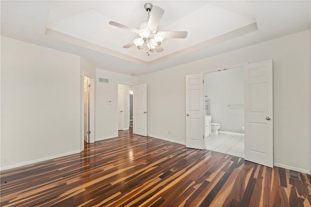 unfurnished bedroom featuring dark hardwood / wood-style floors, ceiling fan, connected bathroom, and a tray ceiling