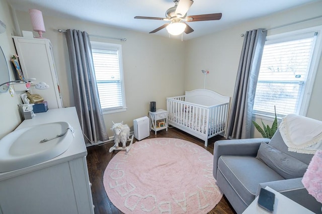 bedroom with ceiling fan, a nursery area, sink, and dark hardwood / wood-style flooring