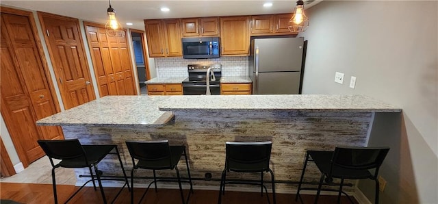 kitchen featuring stainless steel refrigerator, decorative light fixtures, tasteful backsplash, black electric range oven, and a kitchen bar