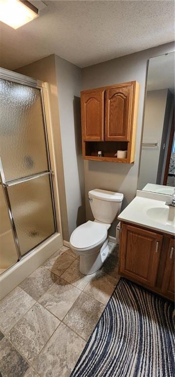 bathroom featuring a shower with door, vanity, a textured ceiling, and toilet