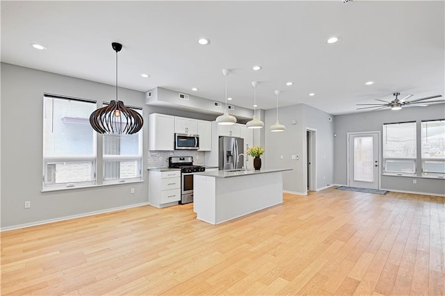 kitchen with open floor plan, stainless steel appliances, hanging light fixtures, and white cabinetry