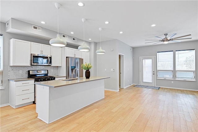 kitchen with white cabinets, appliances with stainless steel finishes, decorative light fixtures, a kitchen island with sink, and light countertops