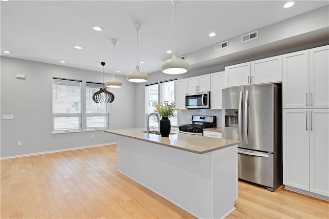 kitchen featuring a center island with sink, visible vents, white cabinets, appliances with stainless steel finishes, and pendant lighting