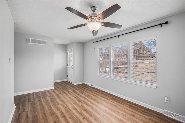 unfurnished room with a textured ceiling, wood finished floors, visible vents, and baseboards