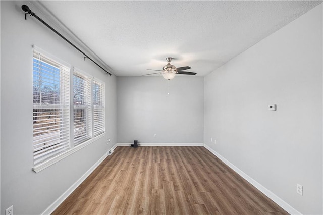 empty room with a ceiling fan, a textured ceiling, baseboards, and wood finished floors