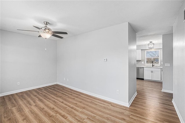 empty room featuring a textured ceiling, a sink, a ceiling fan, baseboards, and light wood-type flooring