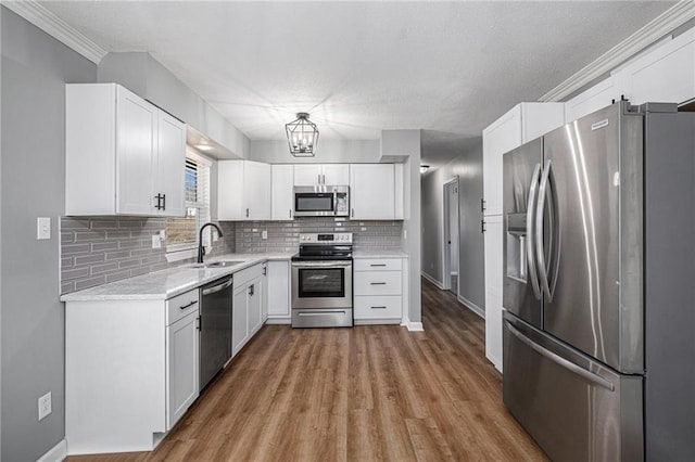 kitchen featuring white cabinets, appliances with stainless steel finishes, wood finished floors, a sink, and backsplash