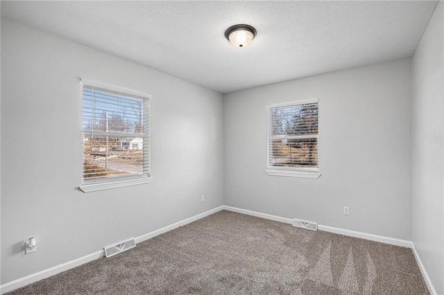 carpeted spare room with visible vents, a textured ceiling, and baseboards