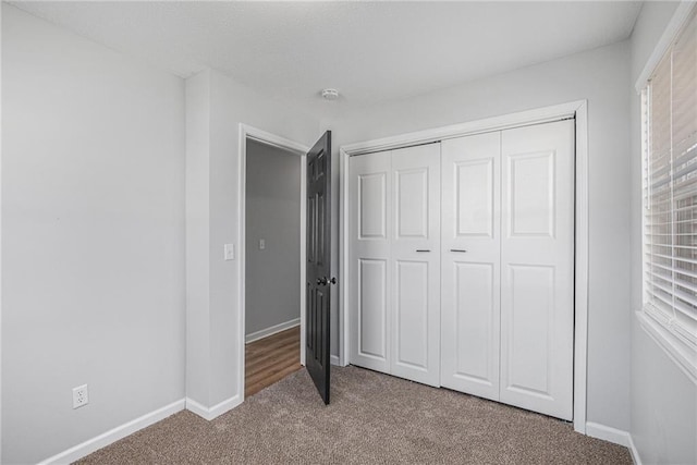 unfurnished bedroom featuring carpet floors, multiple windows, baseboards, and a closet