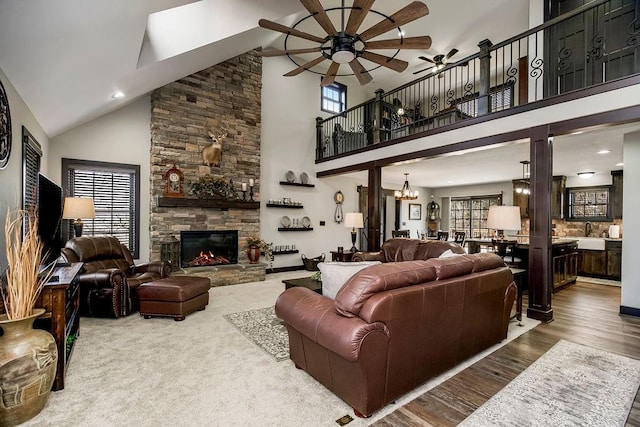 living room featuring a stone fireplace, ceiling fan with notable chandelier, wood-type flooring, sink, and a high ceiling